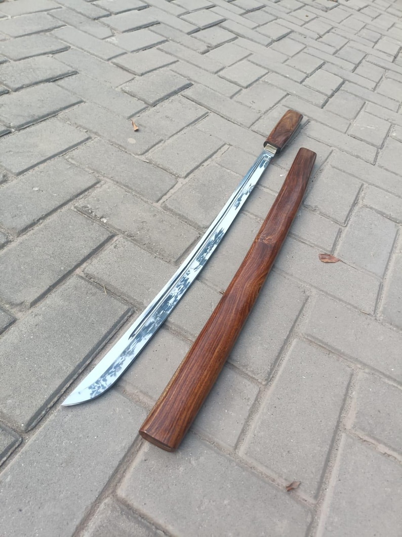 May include: A traditional sword with a polished steel blade and a wooden handle, resting beside its matching wooden scabbard. The blade has a curved edge. The scabbard and handle are a rich, dark brown color.
