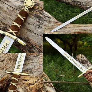 May include: A collection of Viking swords with silver blades, gold accents, and brown leather-wrapped handles. The blades feature engraved text. The swords are displayed on a wooden log.