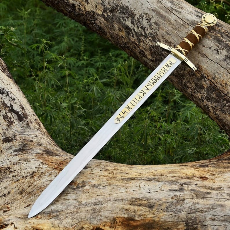 May include: A long, silver sword with a brown leather-wrapped handle and gold accents. The blade features engraved text and rests on a weathered log against a backdrop of green foliage. The sword's design suggests a historical or fantasy theme.
