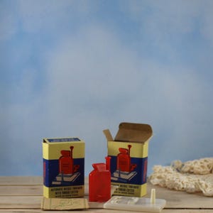 May include: Two boxes and a red plastic needle threader with thread cutter. The boxes are yellow and blue with a red illustration of the threader. The text on the box reads "AUTOMATIC NEEDLE THREADER WITH THREAD CUTTER".