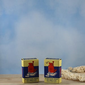 May include: Two vintage automatic needle threader boxes. The boxes are yellow with blue and red graphics. The text on the boxes reads "AUTOMATIC NEEDLE THREADER WITH THREAD CUTTER MADE IN HONG KONG."