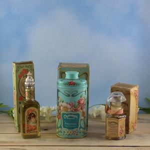 May include: A collection of vintage California Perfume Co. items, including perfume bottles and a powder tin. The products display floral patterns and the brand's logo. The colour scheme features blues, pinks, and greens, with gold detailing.