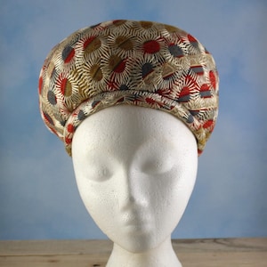 May include: A vintage-style hat with a floral pattern in red, gold, and gray. The hat is displayed on a white mannequin head against a blue background. The hat's design features a repeating pattern of stylized flowers.