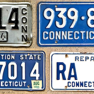 May include: Four vintage Connecticut license plates. The plates are in various conditions, with different color schemes and years. One plate is silver with black lettering, while the others are blue and white. The plates display numbers and the word "Connecticut".