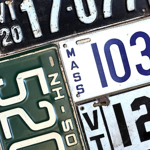 May include: A collection of vintage license plates, featuring various states. The plates display numbers and letters in white and blue against backgrounds of black, green, and white. Some plates show signs of wear and tear, adding to their antique charm.