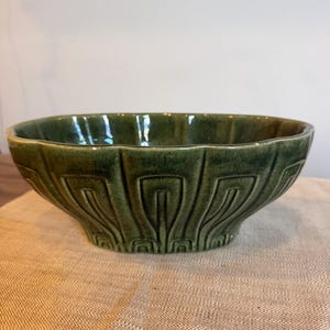 May include: A deep green ceramic bowl featuring a glossy finish and a repeating embossed geometric pattern around the exterior. The bowl has a wide, open top with a scalloped rim and a tapered base, showcasing a consistent dark olive glaze.