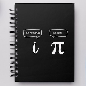 May include: Black spiral-bound notebook with white text and graphics. The notebook cover features the text "Be rational" above the imaginary number "i" and "Be real" above the mathematical constant "π".