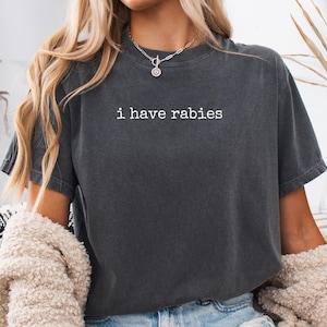 May include: A dark gray t-shirt with the phrase "i have rabies" printed in white. The shirt is a short-sleeved, casual style. The word "PEPPER" is printed in the bottom right corner of the image.