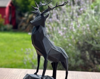 May include: A black, geometric deer sculpture standing on a rocky base. The deer has a detailed, angular design and is made of a 3D printed material.