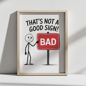 Peut inclure: Impression encadrée avec un bonhomme allumette pointant vers un panneau rouge indiquant "BAD". Le texte au-dessus du panneau dit "THAT'S NOT A GOOD SIGN!". L'œuvre est minimaliste, avec un fond blanc et un cadre en bois.