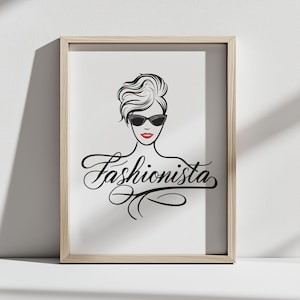 Puede incluir: Impresión enmarcada con una ilustración en blanco y negro de una mujer con gafas de sol y la palabra "Fashionista" en escritura cursiva. La mujer tiene pintalabios rojo. El marco es de color madera clara.