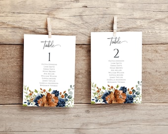 May include: Two white cards with floral designs and the text "Table 1" and "Table 2" with a list of names underneath each table number.