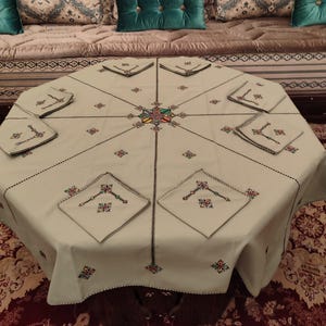 Könnte beinhalten: Ein hellgrüner Tischdecke mit passenden Servietten, bestickt mit bunten geometrischen Mustern. Die Tischdecke liegt auf einem niedrigen Tisch, darunter ein gemusterter Teppich. Die Servietten sind um den Tisch herum platziert.
