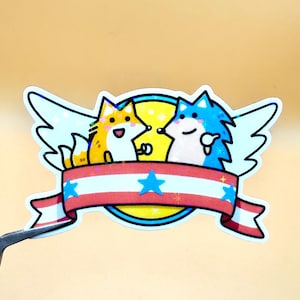 May include: A sticker featuring two cartoon animals, a fox and a hedgehog, with a banner. The fox is orange and the hedgehog is blue. The banner is red and white with blue stars. The sticker has a holographic, glittery effect.