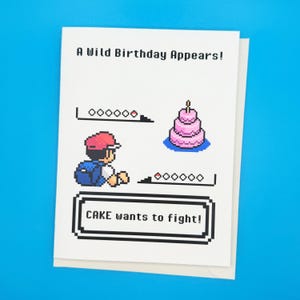 May include: White birthday card with pixelated graphics and text. The card reads "A Wild Birthday Appears!" and "CAKE wants to fight!" with a pink cake and a character in a red hat. The card is on a blue background.