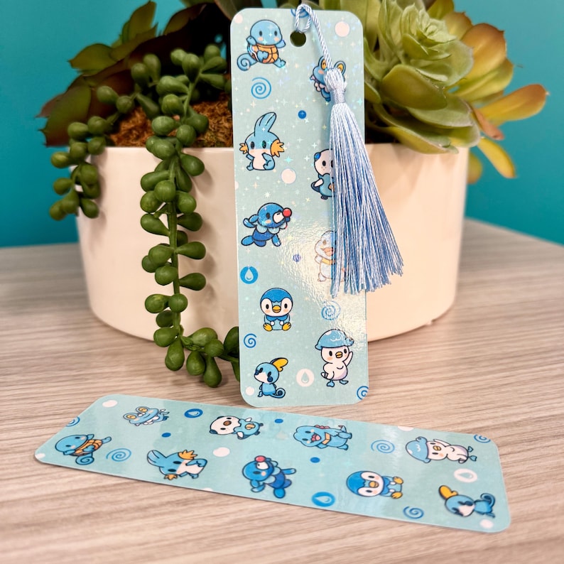 Puede incluir: Dos marcap&aacute;ginas azules con personajes de dibujos animados. Un marcap&aacute;ginas tiene una borla y una cuerda azules. Los marcap&aacute;ginas tienen un fondo azul claro con personajes de dibujos animados y remolinos. Los marcap&aacute;ginas est&aacute;n sobre una superficie de madera clara.