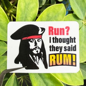May include: A rectangular sticker featuring a black and white illustration of a pirate with a red bandana and a black hat. The sticker has the text "Run? I thought they said RUM!" in red and yellow.