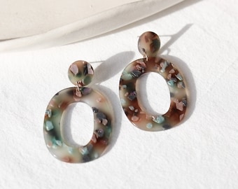May include: A pair of oval-shaped earrings with a brown, white, and green speckled pattern. The earrings have a gold-tone post.