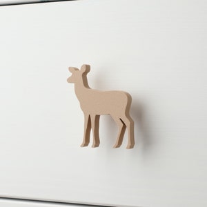 May include: A light brown wooden deer shaped drawer pull. The deer is standing on a white surface.