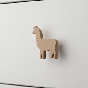 May include: A light brown wooden llama drawer pull. The llama is standing on a white surface.