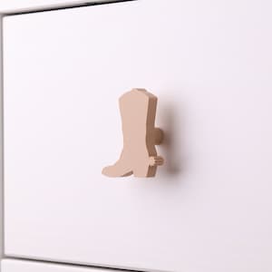 May include: A light brown wooden cowboy boot drawer pull with a spur detail.