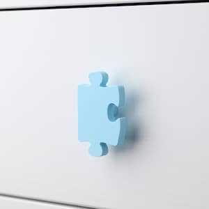 May include: A light blue puzzle piece shaped drawer pull for a white dresser.