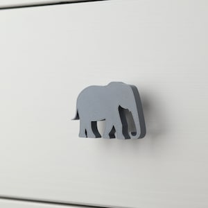 May include: A grey elephant-shaped drawer pull. The pull is made of a textured material and is attached to a white drawer front.