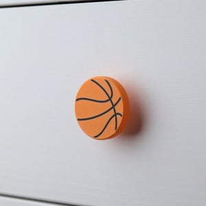 May include: Orange and black basketball-shaped drawer pull for a white dresser.