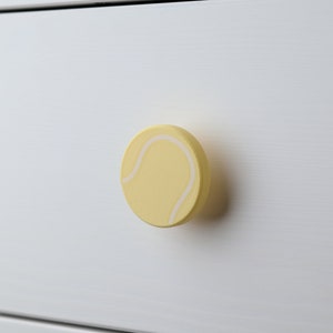 Peut inclure: Une poignée de tiroir en forme de balle de tennis jaune avec des coutures blanches.