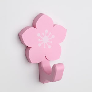 May include: Pink flower-shaped wall hook with a white flower design.