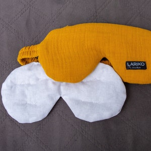 May include: Mustard yellow sleep mask with an elastic band, and a white eye mask. The sleep mask has the text "LARIKO STUDIO" on a black label. The eye mask is white and has a stitched design.