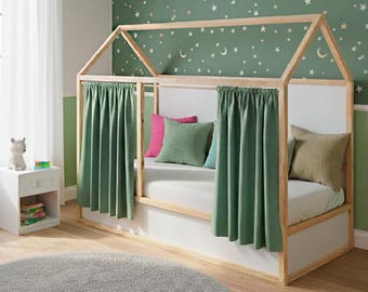 May include: A wooden house-shaped bed frame with white panels and green curtains. The bed is furnished with pillows in shades of pink, green, and blue. The room has a green wall with a star and moon pattern.