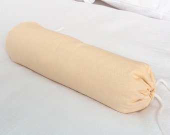 May include: A beige cylindrical pillow with a white drawstring closure, lying on a white bed.