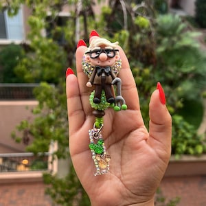 Könnte beinhalten: Ein handgefertigtes Ausweis-Jojo mit einer Miniaturfigur eines älteren Mannes mit Brille, Fliege und Gehstock. Die Figur ist mit glitzernden Verzierungen versehen. Das Jojo enthält einen transparenten Kunststoffabschnitt mit zusätzlichen dekorativen Elementen.