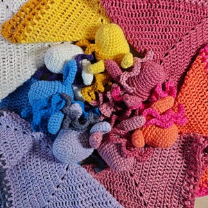 May include: A collection of colorful crochet items, including blankets and small octopus-shaped toys. The blankets are in shades of white, blue, purple, yellow, pink, and orange. The octopus toys are in blue, yellow, pink, and purple.