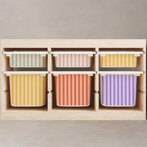 May include: A wooden storage unit with six colorful striped bins. The bins are in shades of yellow, orange, pink, purple, and green. Each bin has a white lid. The unit is made of light-colored wood.