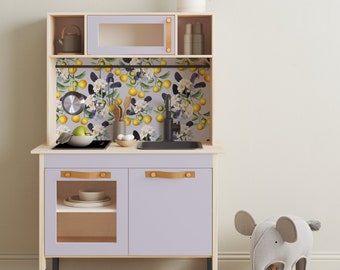 May include: A light purple toy kitchen playset with a floral patterned backsplash, a microwave, a sink, and two cabinets. The kitchen has a black stovetop and a black sink. The kitchen is on black legs. A gray elephant toy is in the foreground.