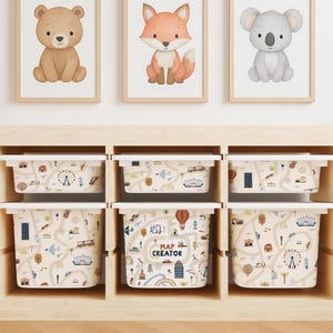 May include: A wooden storage unit with six bins, each with a white lid and a beige map design. Above, framed watercolor prints of a bear, fox, and koala bear decorate the wall. The text "LET'S PLAY! MAP CREATOR" is visible on one bin.