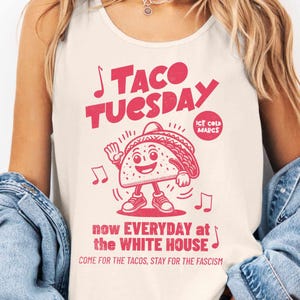 May include: Ivory tank top with a red graphic that reads "TACO TUESDAY" with a cartoon taco character and musical notes. The text "now EVERYDAY at the WHITE HOUSE" and "COME FOR THE TACOS, STAY FOR THE FASCISM" are also included.