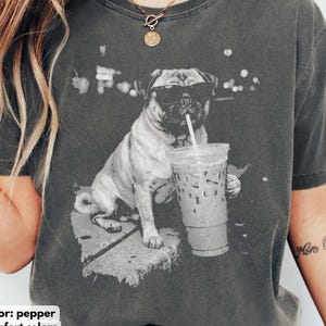 May include: Pepper-colored Comfort Colors t-shirt featuring a black and white graphic of a pug wearing sunglasses and drinking an iced coffee. The shirt has the words "color: pepper comfort colors" printed at the bottom.