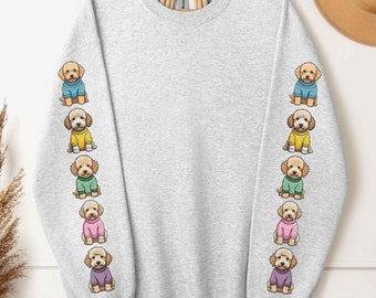 May include: A gray sweatshirt with a row of cartoon dogs wearing colorful sweaters on each sleeve. The sweatshirt is a light gray color and the dogs are all facing forward. The text "ash" is printed in black at the bottom left of the image.