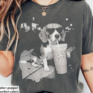Puede incluir: Camiseta color pimienta con un dibujo en blanco y negro de un beagle con gafas de sol bebiendo un caf&eacute; helado. El perro est&aacute; sentado en una repisa. Las palabras "color: pepper" y "comfort colors" est&aacute;n en la parte inferior.