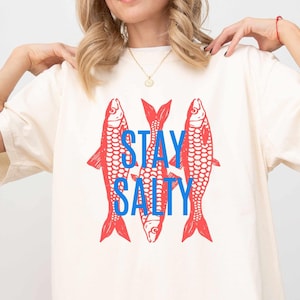 May include: A white oversized t-shirt with a graphic of three red fish and the text "STAY SALTY" in blue.