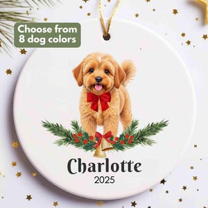 May include: A white ceramic Christmas ornament featuring a golden retriever-type dog with a red bow, surrounded by greenery and bells. The name "Charlotte" and the year "2025" are printed below. Text reads "Choose from 8 dog colors".