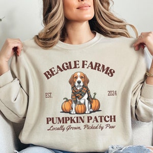 May include: Beige sweatshirt with a brown graphic of a beagle dog sitting with pumpkins and the text "BEAGLE FARMS EST. 2024 PUMPKIN PATCH Locally Grown. Picked by Paw"