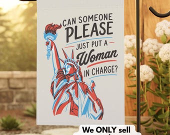 May include: A white garden flag with the Statue of Liberty in red and blue, holding a torch. The flag has the text "CAN SOMEONE PLEASE JUST PUT A WOMAN IN CHARGE?" and "We ONLY sell progressive gear."