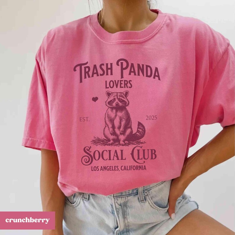 May include: Pink t-shirt with a graphic of a raccoon and the text "Trash Panda Lovers Social Club Los Angeles, California" printed on it.