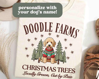 May include: A cream-colored t-shirt with a doodle dog wearing a red and green sweater in front of a Christmas tree. The text "Doodle Farms Christmas Trees Locally Grown, Cut by Paw" is printed on the shirt.