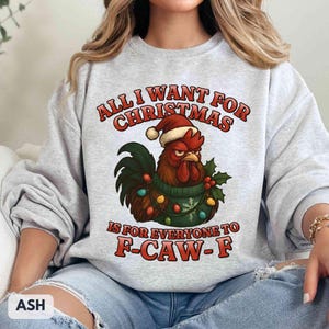 May include: Ash gray sweatshirt with a Christmas rooster graphic. The rooster wears a Santa hat and a green sweater with Christmas lights. Text reads "ALL I WANT FOR CHRISTMAS IS FOR EVERYONE TO F-CAW-F."
