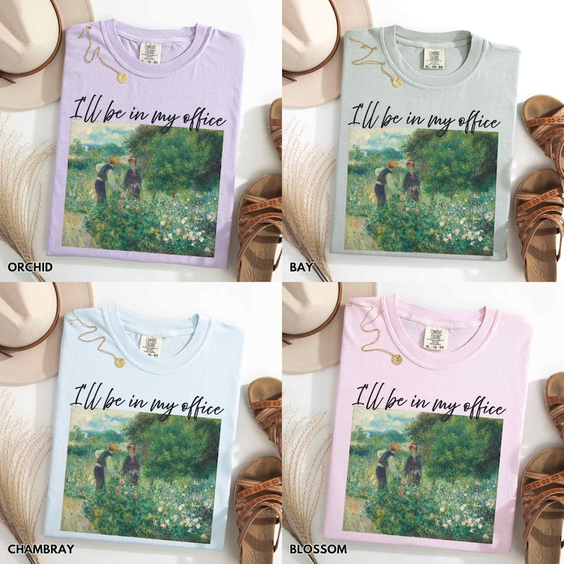 May include: Four pastel-coloured t-shirts: orchid, bay, chambray, and blossom. Each features the phrase "I'll be in my office" and a painting of two figures in a field. Gold necklaces, hats, and sandals are also visible.